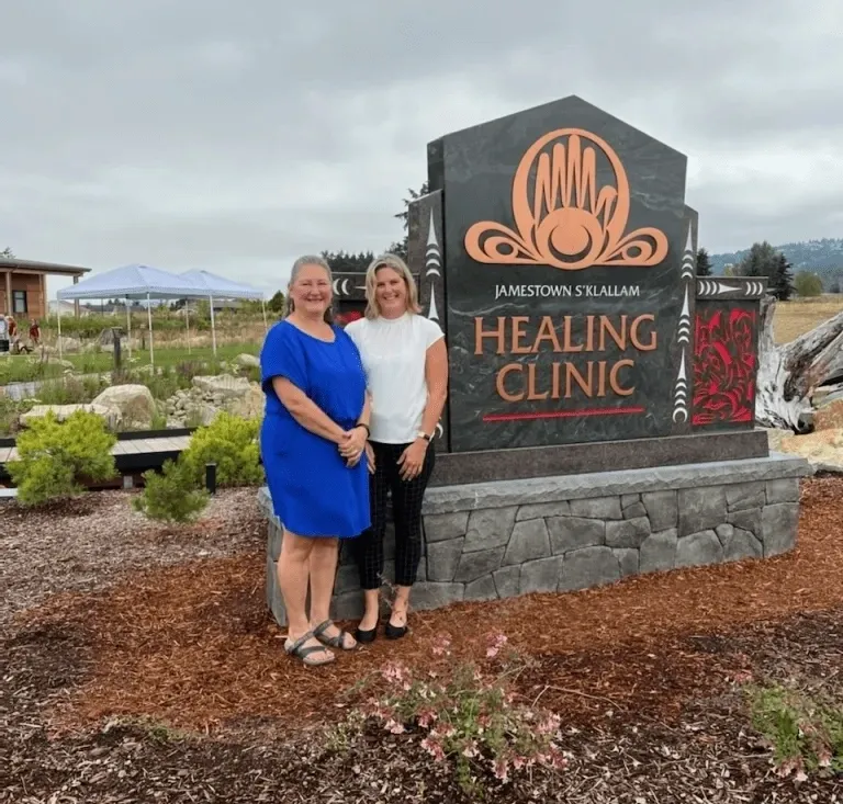 Two women standing in front of a sign for the healing clinic.